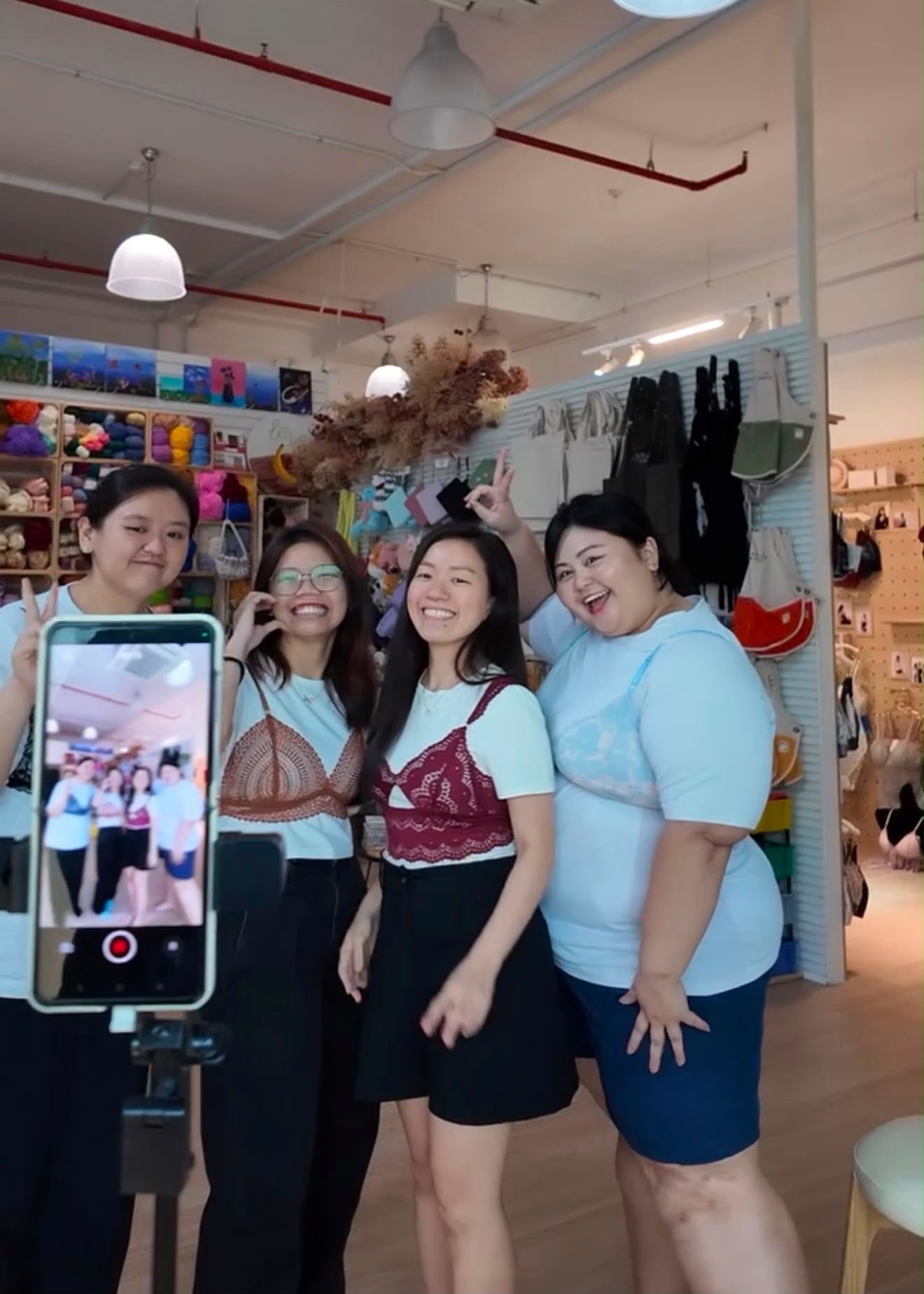 Four happy friends posing together in a bright craft studio showing off their custom sewing projects during a group team bonding workshop.