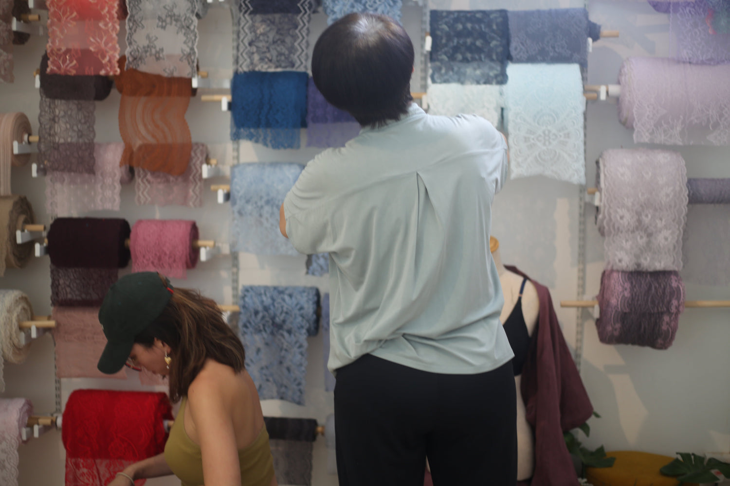 A mother and daughter selecting luxury lace fabrics from a display wall during a private intimate wear sewing workshop