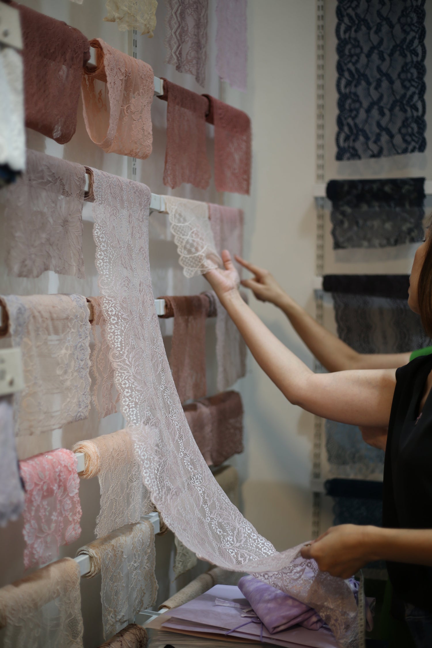 Corporate workshop participants browsing a rack of luxury stretch laces to select materials during a 7-pax team bonding lingerie sewing session.