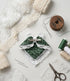 Flat lay of a DIY craft kit featuring a handmade green patterned fabric hair clip with a white lace bow and trim, surrounded by sewing needles, scissors, thread spools, and lace ribbons