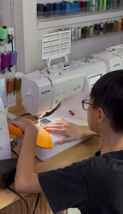 Jeannie, Founder of Envy Her Singapore, guiding a child at the sewing machine during Envy junior Stitch &amp; Sketch kids sewing workshop