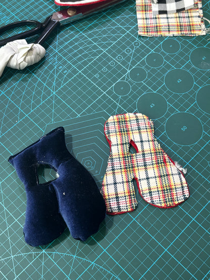 Overhead shot of a self-made initial cushion craft kit displaying completed mini alphabet pillows alongside a wooden spool, measuring tape, scissors, small thread vials, and pins