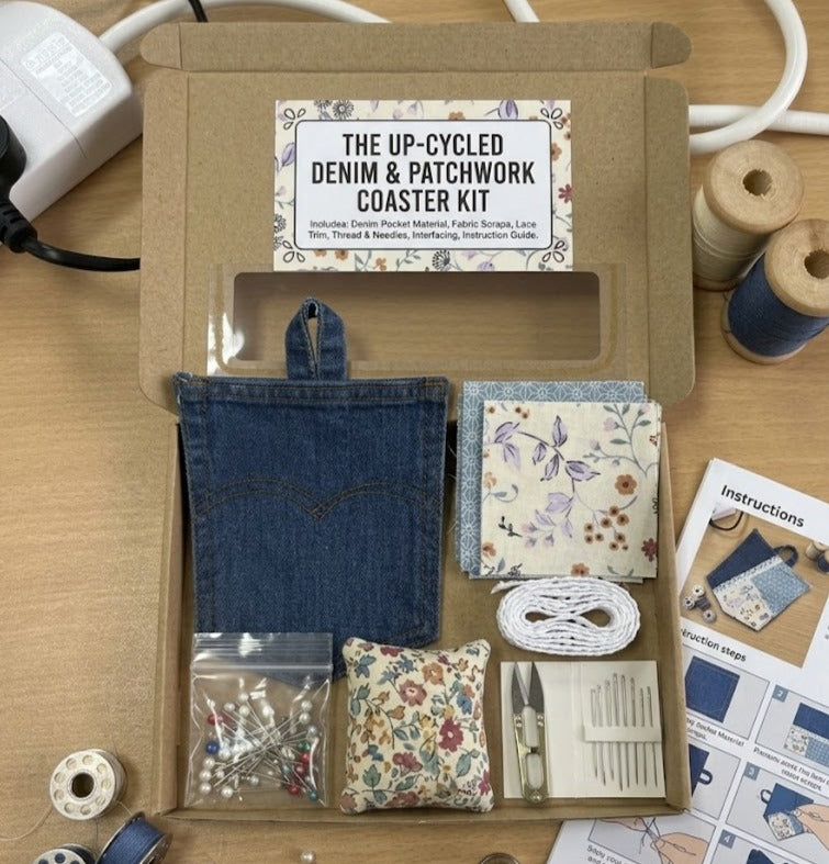 The Up-Cycled Denim and Patchwork Coaster Kit neatly packed in a cardboard box, featuring a denim pocket, pre-cut floral and geometric fabric scraps, lace trim, pins, a pincushion, sewing needles, thread snips, and a printed instruction guide
